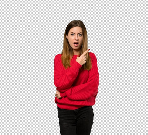 驚いて側を指している赤いセーターを持つ若い女