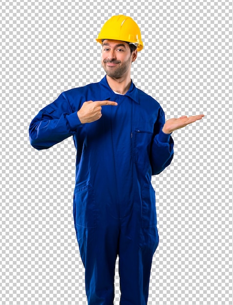 Young workman with helmet holding copyspace imaginary on the palm to insert an ad
