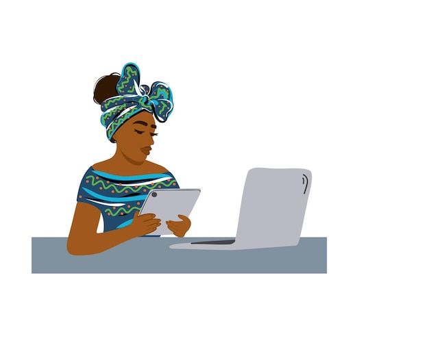 Afro-Amerikaanse vrouw in nationale kleding zit aan een tafel met een laptop en houdt een tablet vast