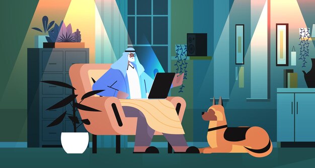 Arab senior man using laptop arabic grandfather with dog working in dark night living room