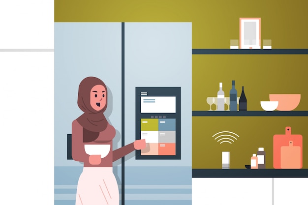 arab woman touching refrigerator screen with smart speaker voice