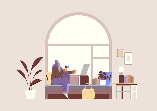 Arab woman with credit card using laptop online shopping concept living room interior horizontal