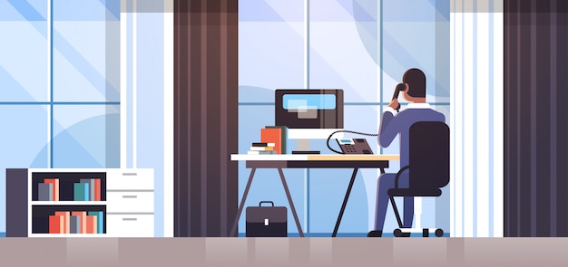 Vector businessman sitting at workplace desk rear view business man using computer while talking on landline phone working process concept creative office interior  horizontal