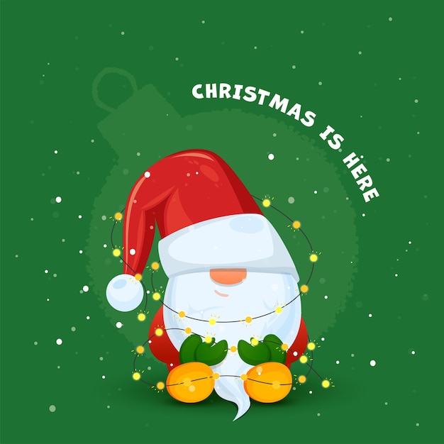 Christmas Is Here Font With Cartoon Gnome Wearing Santa Hat And Lighting Garland On Green Bauble Snowfall Background