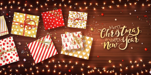 Christmas and new year background with gift boxes, xmas garlands of lights, baubles and glitter confetti on wooden texture.