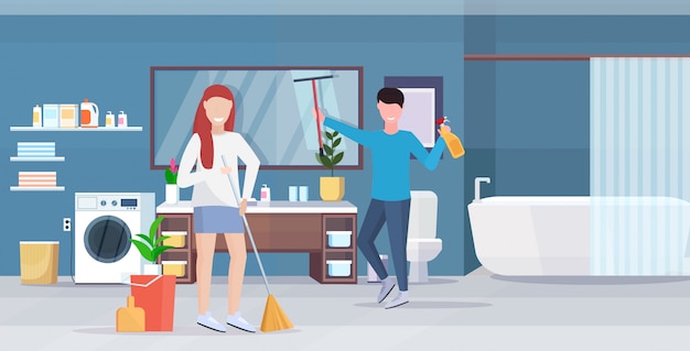 Couple doing housework together man wiping glass mirror woman sweeping floor with broom cleaning housekeeping concept modern bathroom interior full length horizontal