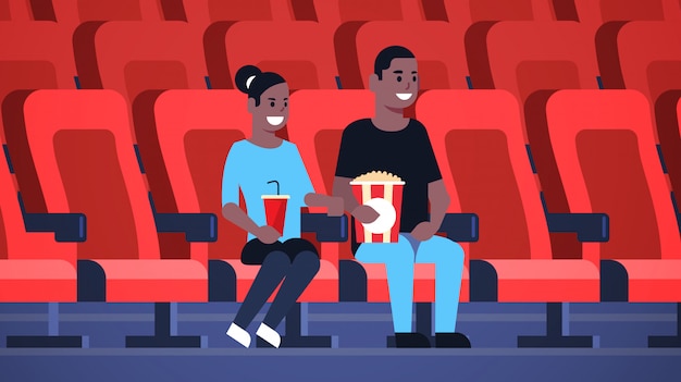 Coppia di guardare film seduto al cinema con popcorn e cola uomo afro-americano donna con data e ridendo di nuova commedia