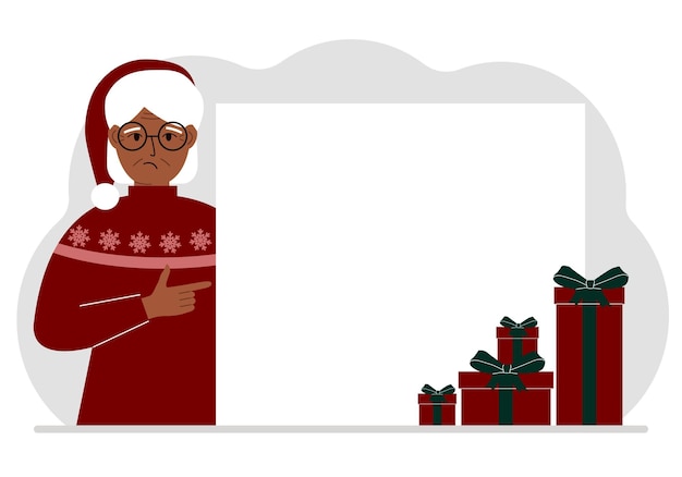 Een oude vrouw in een kerst- of nieuwjaarssweater met een rode sana-pet wijst met zijn vinger naar een spandoek, een blanco poster of een groot wit vel papier met ruimte voor tekst