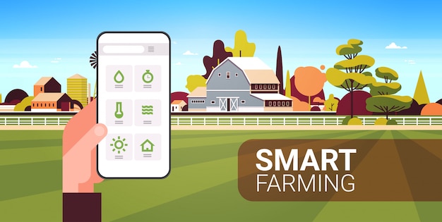 スマートフォンの監視状態を保持している農家の手収穫のスマートファーミングの概念を制御する農産物の組織農場の風景風景の背景水平コピースペース