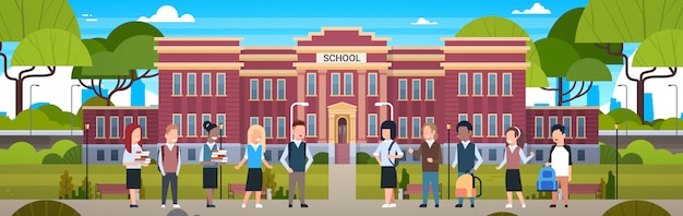 Group of diverse pupils in front of school building studerns on yard with green grass and trees