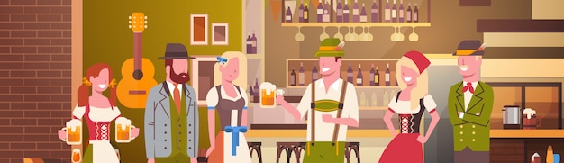 Il gruppo di persone beve la birra nell'uomo e nella donna di celebrazione del partito di oktoberfest della barra che indossano il concetto tradizionale del fest dei vestiti