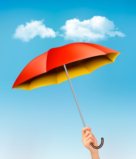 Hand met een rode en gele paraplu tegen een blauwe hemel met wolken.