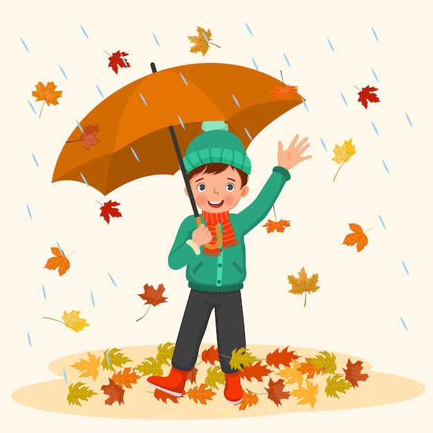 happy little boy holding umbrella under rain with fallen leaves in autumn