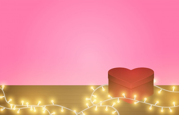 Heart shape box and glowing light on wooden table on pink