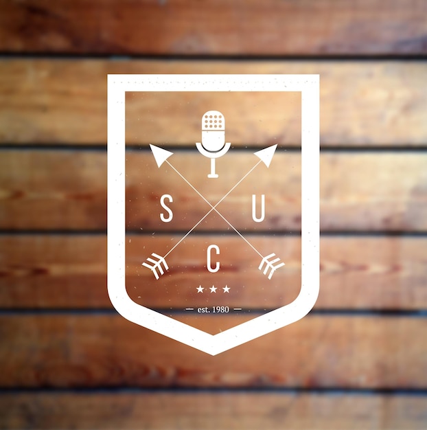 Scudo con logo hipster con frecce incrociate e microfono retrò a podcast in legno sfocato o spettacolo in piedi