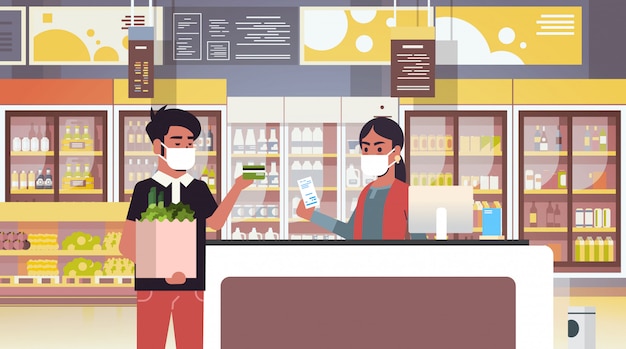 indian cashier and man customer in medical protective masks quarantine coronavirus epidemic concept people buying goods in grocery store supermarket interior portrait horizontal