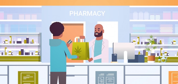 Farmacista maschio di medico che dà il pacchetto medico della cannabis al cliente afroamericano al ritratto orizzontale di concetto interno di sanità della medicina della contro farmacia moderna della contro farmacia