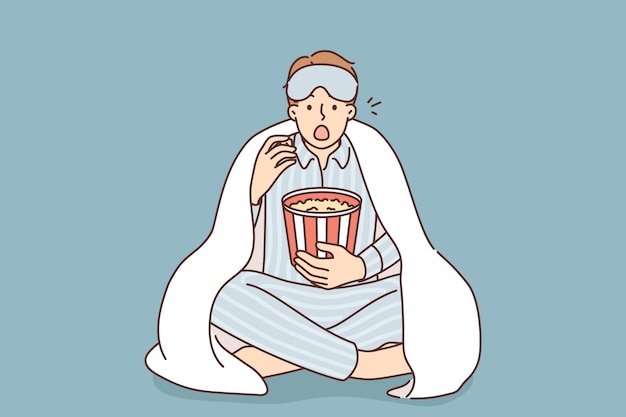 Man in pyjama eet popcorn film kijken