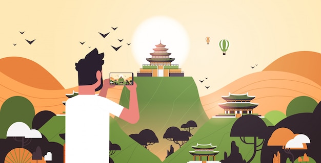 man traveler photographing chinese pagoda in traditional style on smartphone camera