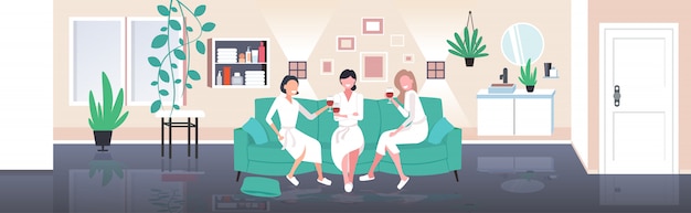 mooie vrouwen in badjassen drinken van wijn plezier thuiszorg concept meisjes ontspannen op de sofa