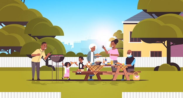 Multi generation family preparing hot dogs on grill african american grandparents parents and children having fun backyard picnic barbecue party concept flat full length horizontal