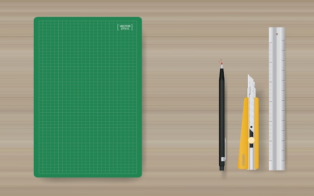 Office object background of green cutting mat with ruler, cutter and pencil on wood.