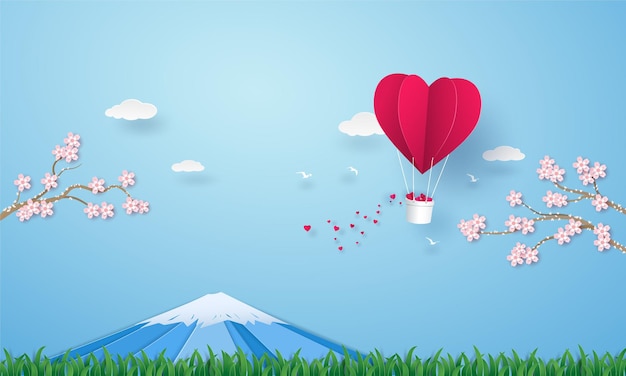 Сердце оригами на воздушном шаре, летящее в небе над травой с горой Фудзи и цветущей вишней.