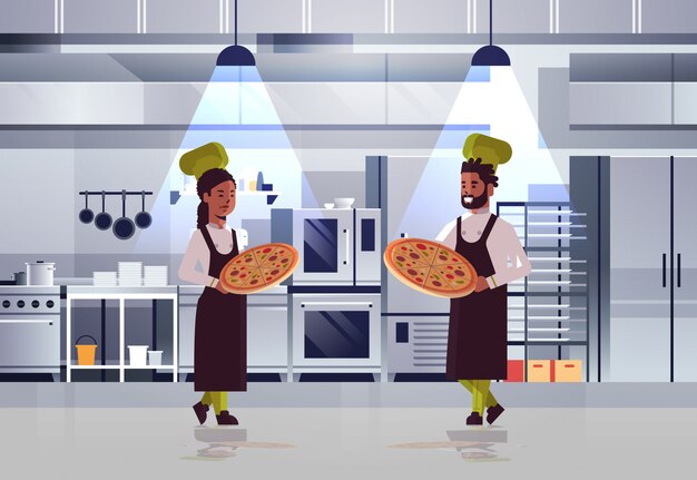 Professional chefs couple holding trays with fresh pizza african american man woman in uniform standing together cooking food concept modern restaurant kitchen interior