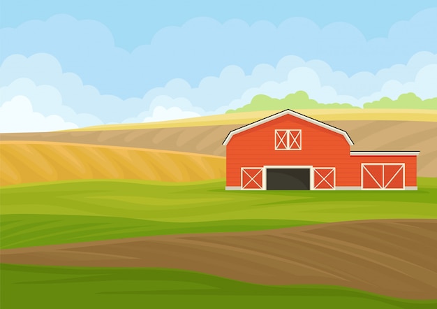 Red wooden shed with garage in a plowed field.