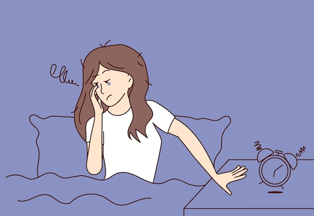 眠くて疲れた女性はベッドに座って目覚まし時計を止めようとします不眠症と戦う