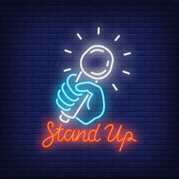 Stand up neon sign. Microphone in human hand on brick wall background. 