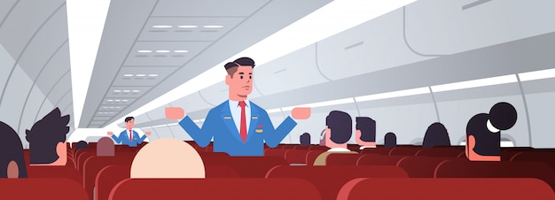 Steward explaining instructions for passengers male flight attendants in uniform showing emergency exits safety demonstration concept airplane board interior horizontal