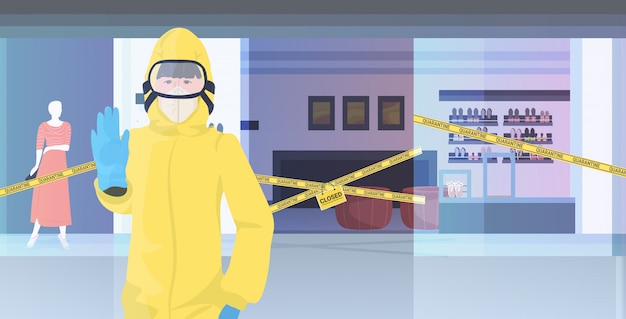 Donna in tuta hazmat mostrando fermata gesto centro commerciale con nastro giallo quarantena pandemia coronavirus