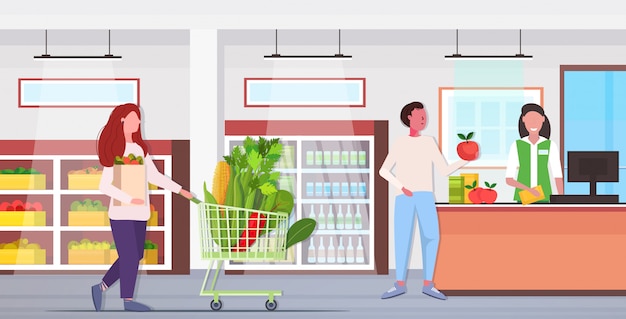 Woman pushing trolley cart with different vegetables healthy lifestyle vegan fresh food concept modern grocery shop interior full length horizontal