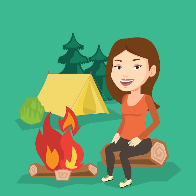 Donna che si siede sul ceppo vicino al fuoco di accampamento nel campeggio.