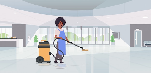 Woman using professional vacuum cleaner   female cleaner janitor in uniform cleaning service floor care concept modern hotel lobby hall interior horizontal  full length