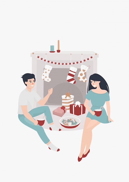 Young couple sits by the fireplace and drinks cocoa surrounded by christmas presents