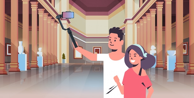 young couple using selfie stick taking photo on smartphone camera man woman visitors in modern art gallery museum hall interior portrait horizontal