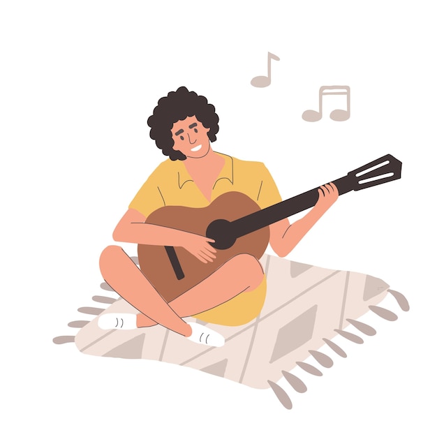 젊은 남자가 담요에 앉아 기타를 치고 있다 남자는 미소를 짓고 노래를 부르고 th를 뽑는다