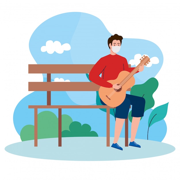 젊은 남자 의료 마스크를 쓰고 공원 의자에 앉아 기타 연주