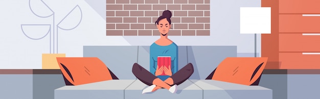 Young woman sitting on couch using tablet girl reading e-book e-learning concept modern