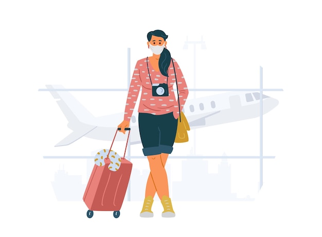Giovane donna che indossa la maschera protettiva con la valigia e la macchina fotografica in piedi in viaggio in aeroporto durante la pandemia concept