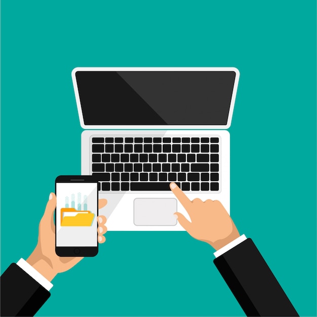 hand holds phone and click on laptop. upload files to the cloud storage or computer. view top of open laptop.