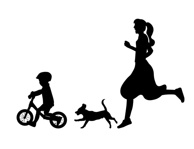 Silhouette of a mother and a dog chasing a child riding a balance bike