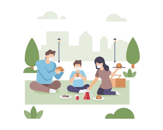 Rodziny jedzą razem w publicznym parku miejskim, nosząc ilustrację maski
