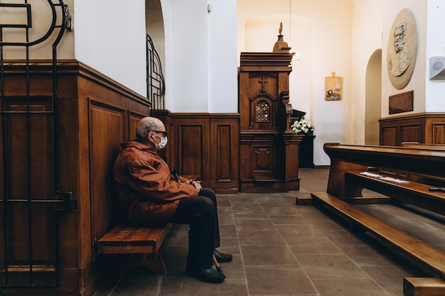 07062020 Winnica Ukraina starszy mężczyzna z kijem w dłoniach i maską na twarzy siedzi na ostatniej ławce w kościele podczas liturgii podczas pandemii koronawirusa