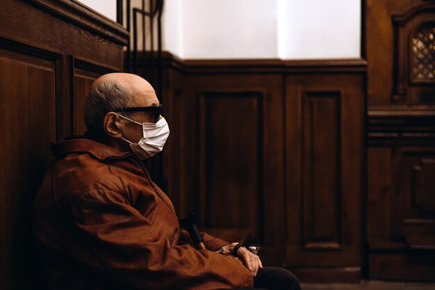 07062020 Winnica Ukraina starszy mężczyzna z kijem w dłoniach i maską na twarzy siedzi na ostatniej ławce w kościele podczas liturgii podczas pandemii koronawirusa