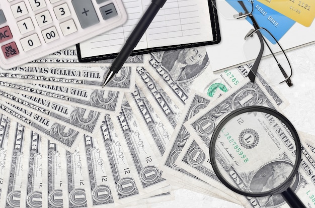 Zdjęcie 1 dolar amerykański i kalkulator z okularami i długopisem. koncepcja sezonu płatności podatku lub rozwiązania inwestycyjne. poszukiwanie pracy z wysokimi zarobkami