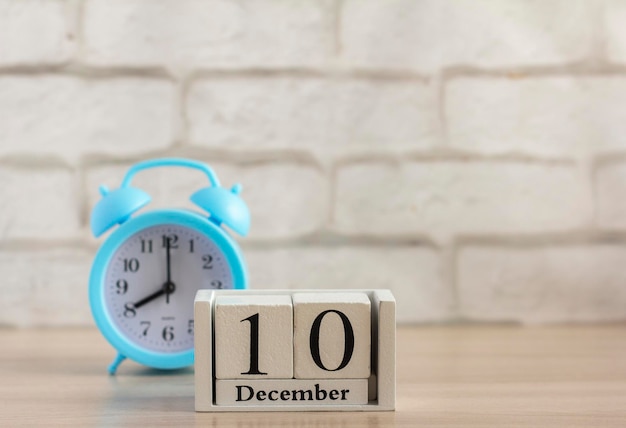 10 grudnia na białym drewnianym kalendarzu i budziku na stole z kopią przestrzeni.