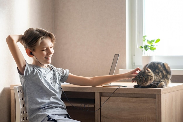 Zdjęcie 11-letni chłopiec siedzi przy stole w swoim pokoju i słucha muzyki przez słuchawki